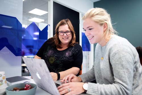 to personer sitter foran en PC-skjerm og smiler.
