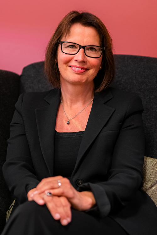 Portrett av Solfrid sittende i en svart sofa foran en rosa vegg.