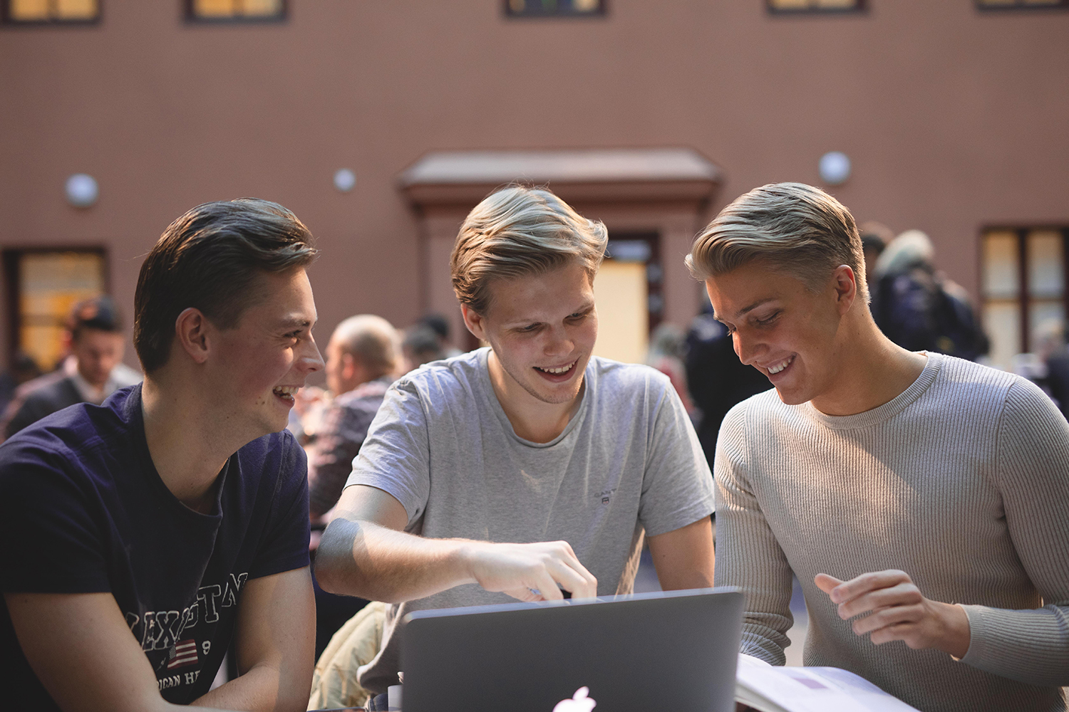 Foto av tre unge mannlige studenter samlet foran en laptop.