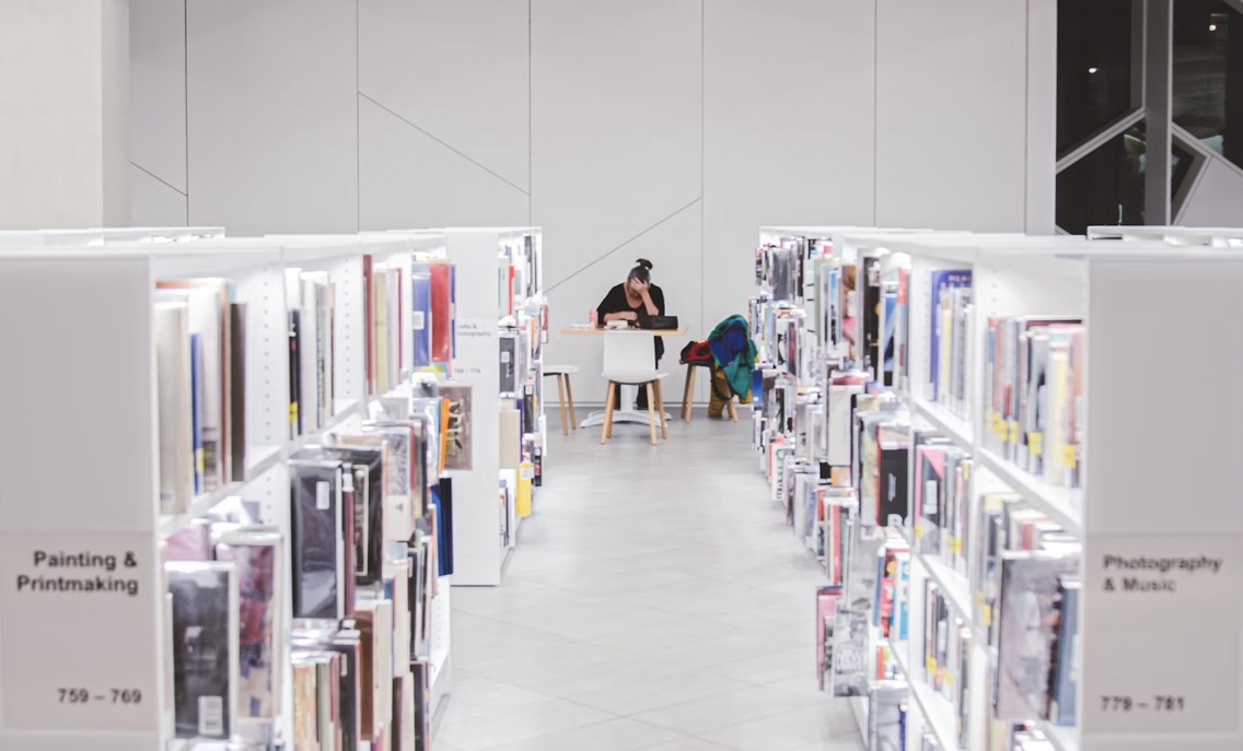 En kvinne som sitter i enden av en biblioteksgang som leser en bøk i et universitetsbibliotek.