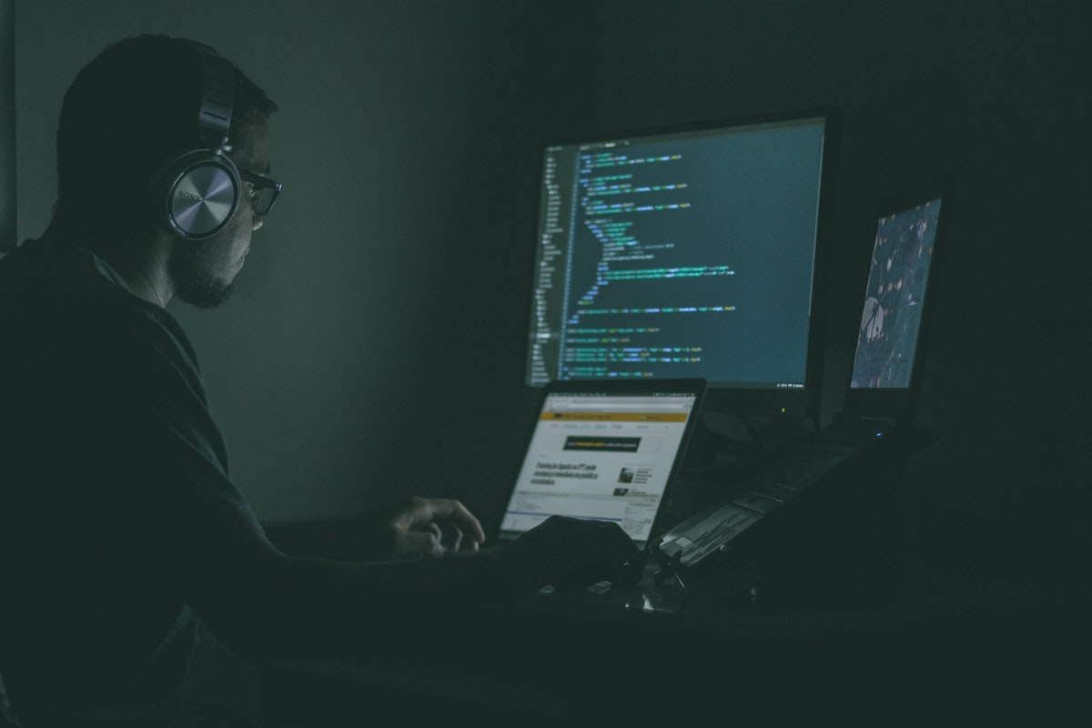 En ung mann sitter i en mørkt rom og jobber på PC-en. 