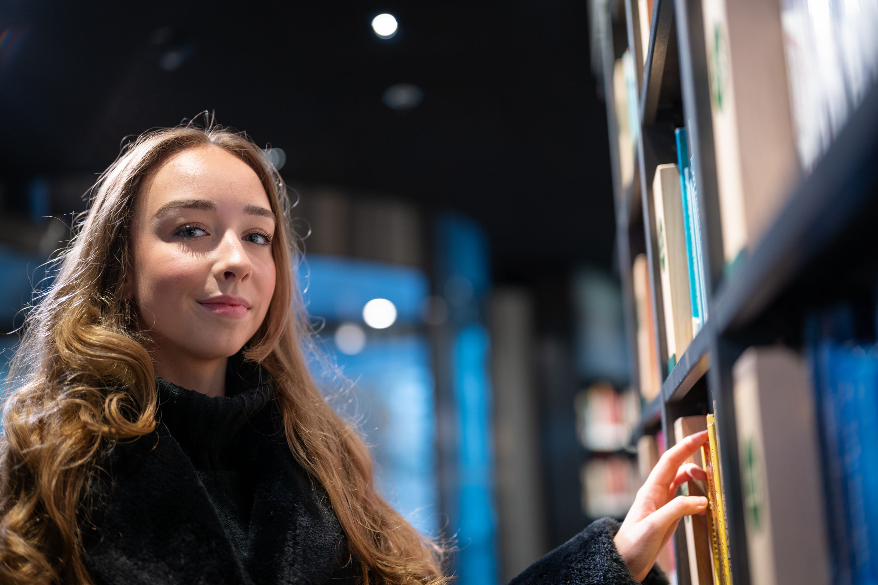 Karine står foran en bokhylle.