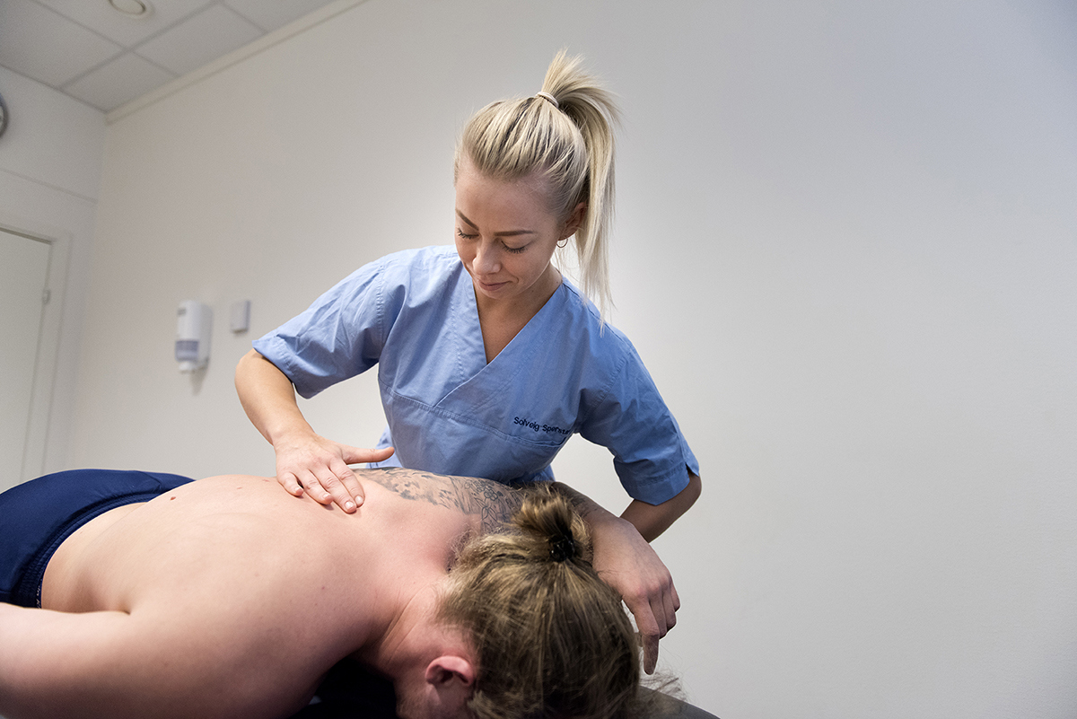 Kvinnelig osteopat i uniform som behandler skulderen til en mann.