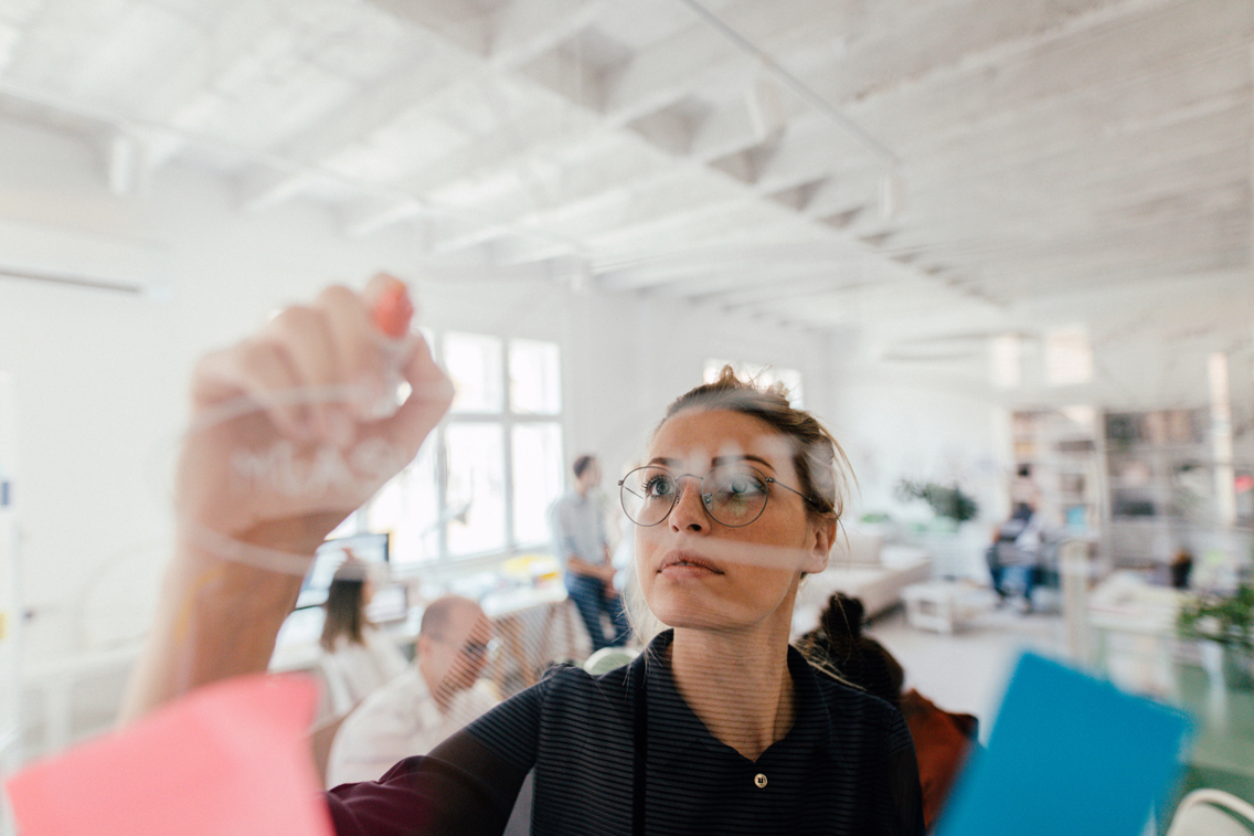Young woman writing on a transparent wipe board and thinking of a solution for her work-related problems.