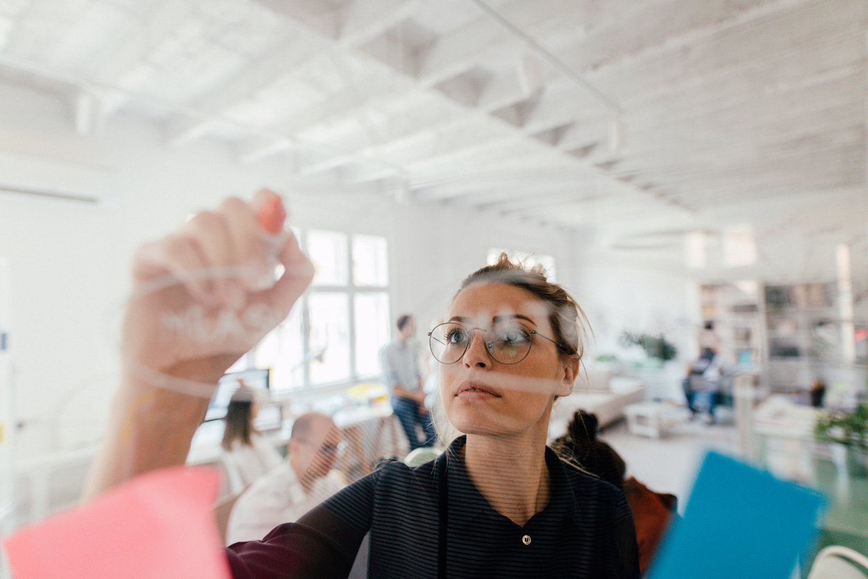 Young woman writing on a transparent wipe board and thinking of a solution for her work-related problems.