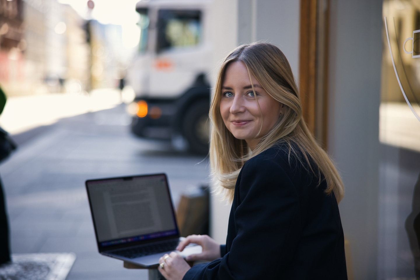 Portrett av Mathilde Hogsnes på en benk i bymiljø, mens hun skriver på en avhandling.