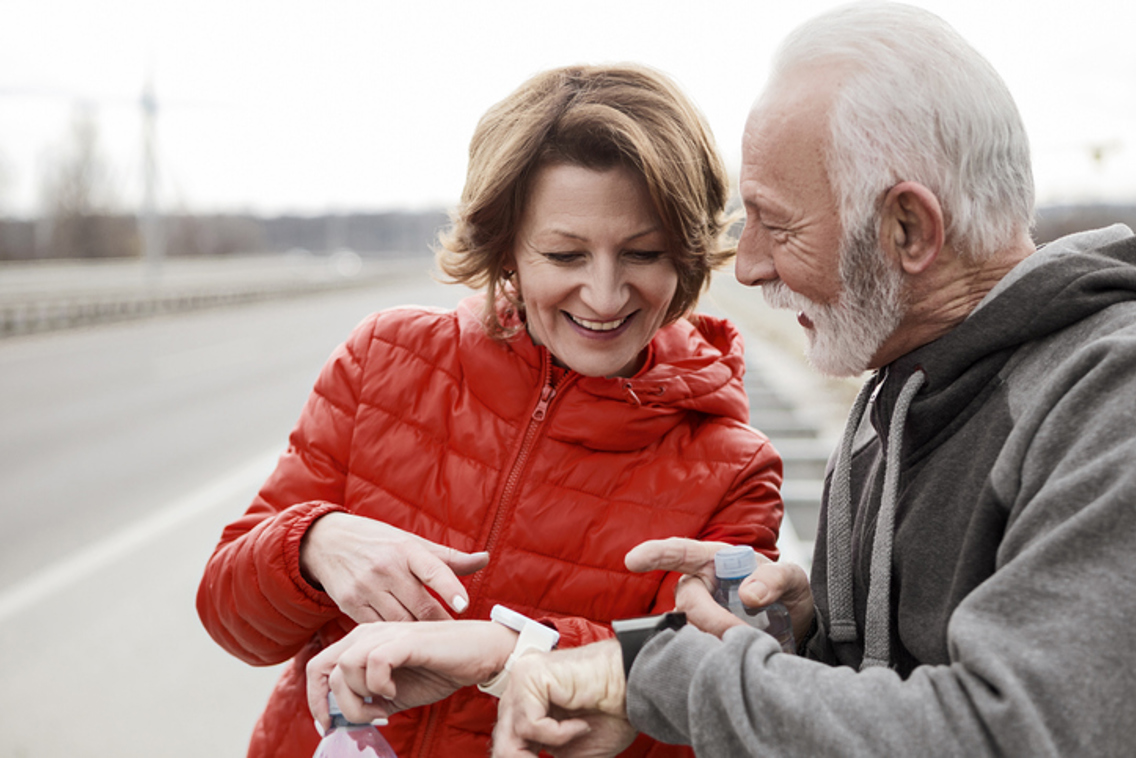 Middelaldrende par som smiler og ser på hverandres smartklokker