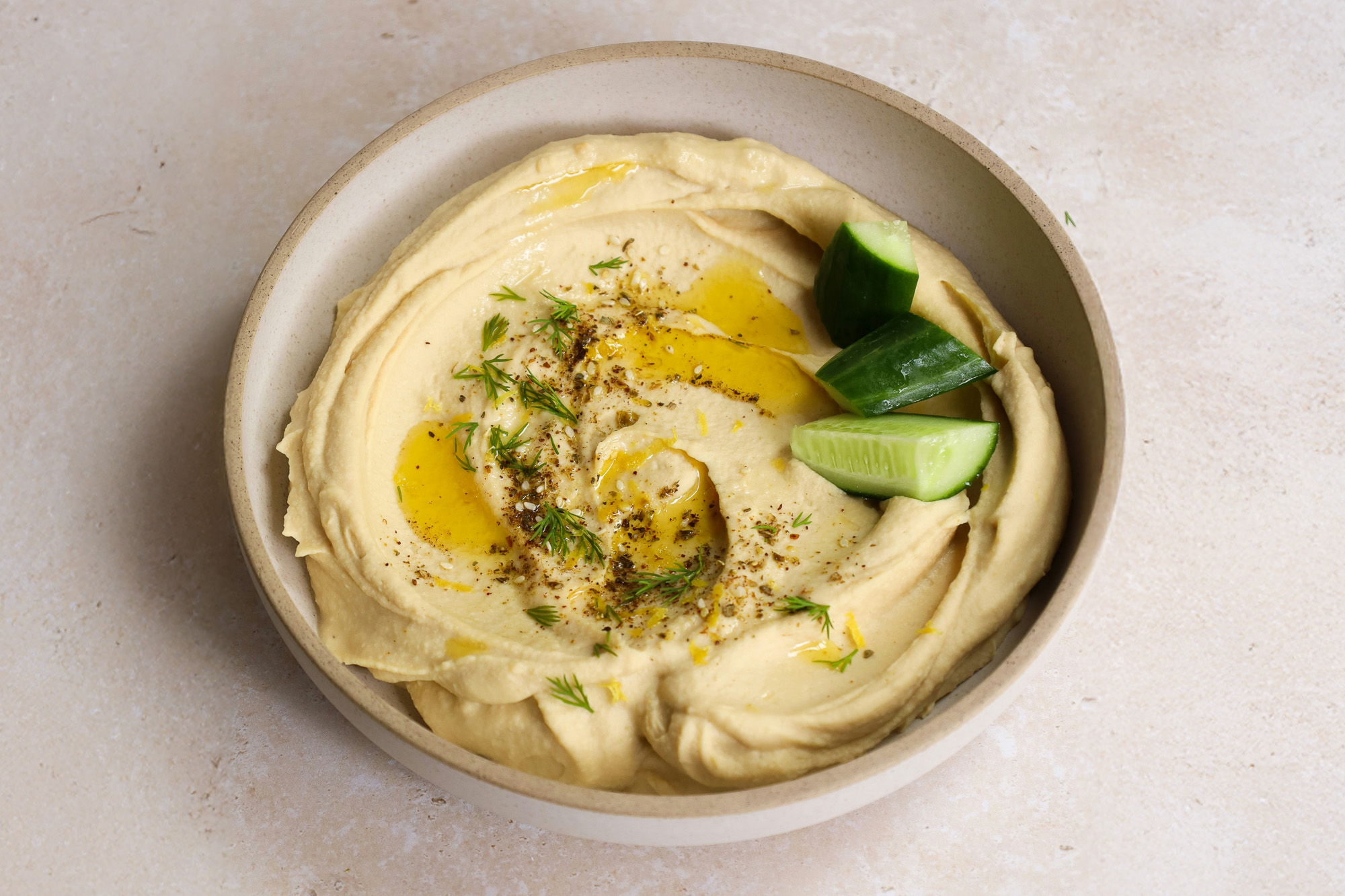 Skål med hummus som er toppet med agurk