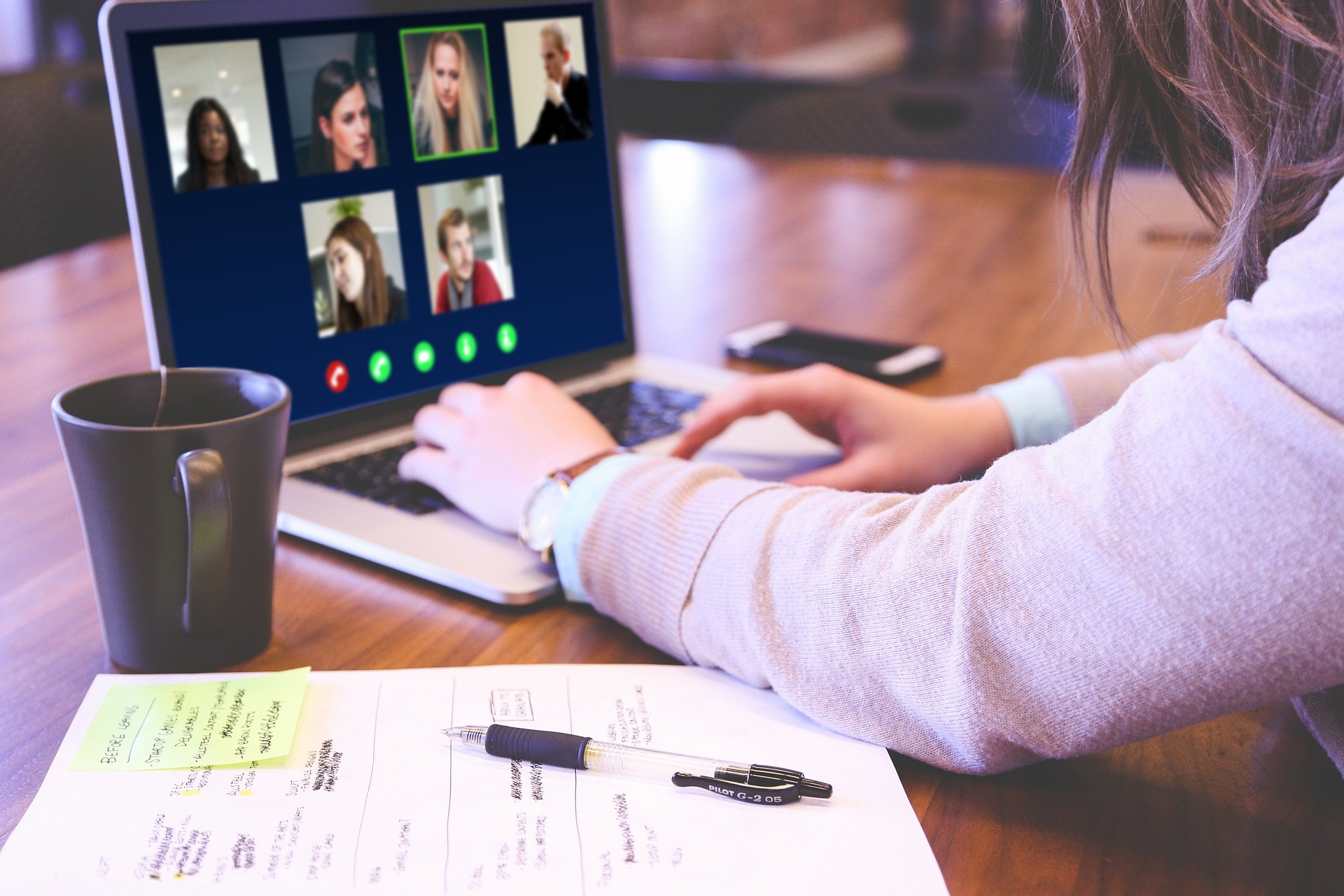 En person sitter med en bærbar PC på et bord. På PCen ser man bilder av flere personer. Det foregår en videokonferanse.