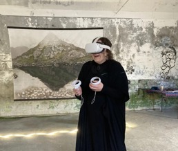 En kvinne står med VR-briller og kontroller i et stort rom