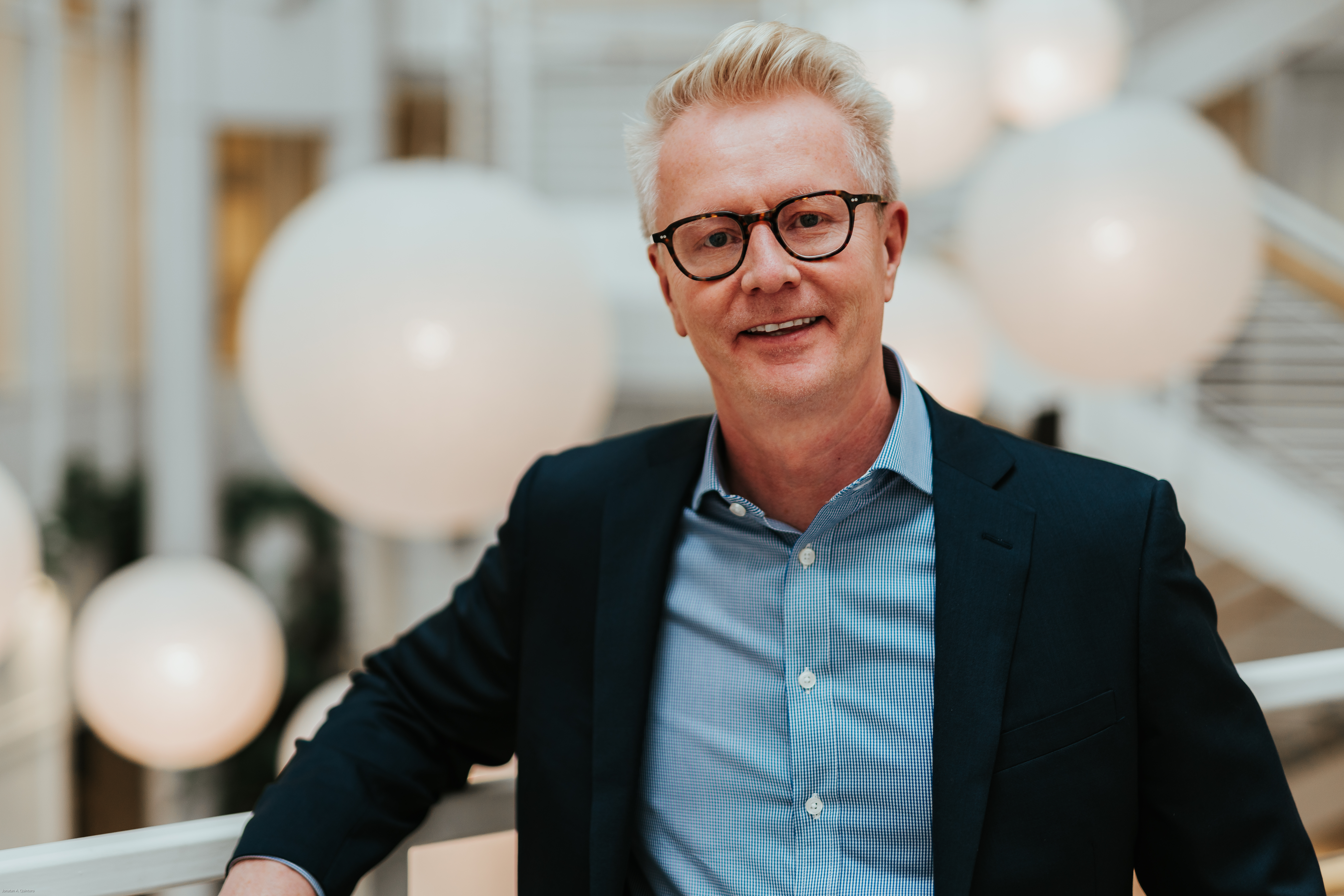 Foto av voksen mann med briller i blå skjorte og sort dressjakke.