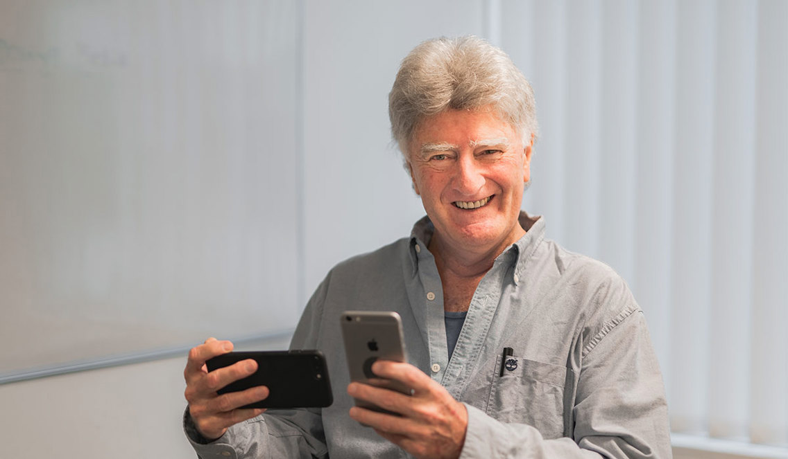 Voksen mann holder en mobil i hver hånd.
