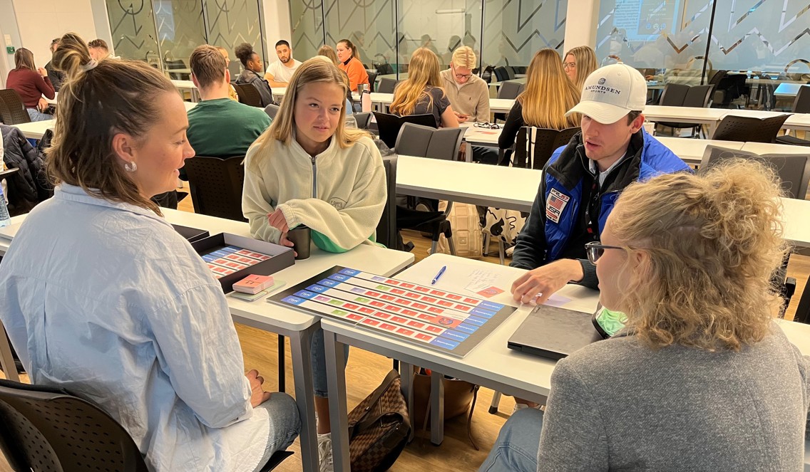 Fire studenter sitter rundt et bord og spiller brettspill