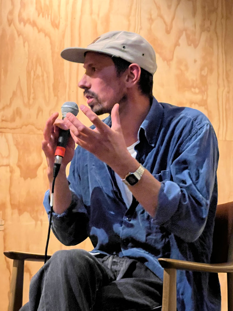 Mann med caps på hode gestikulerer inn i en mikrofon.