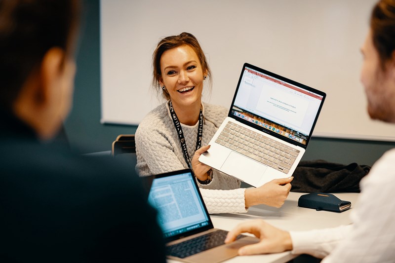 Foto av kvinnelig student som viser frem laptop-skjermen til to andre.