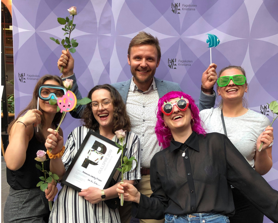 Geir Arne Jacobsen står foran en lilla fotovegg sammen med fire kvinnelige studenter fra Prosjektledelse. De har på seg party-effekter og smiler. 