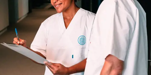 To personer i sykepleieruniform snakker sammen. Man ser ikke ansiktene deres.