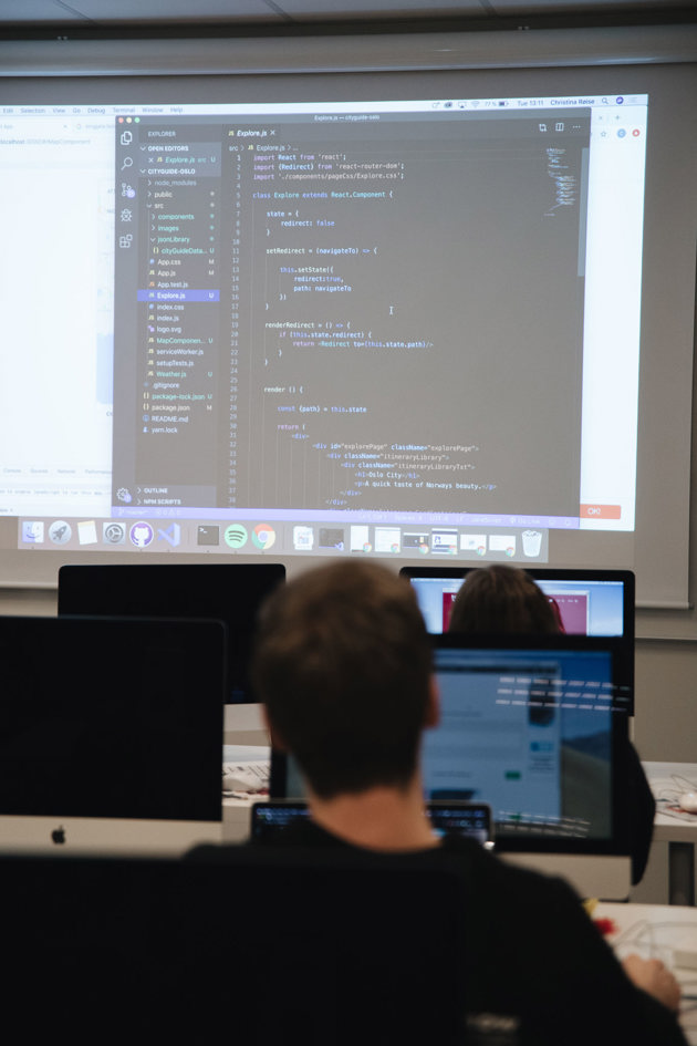 Studenter sitter i klasserommet og følger med på koding på storskjerm. 