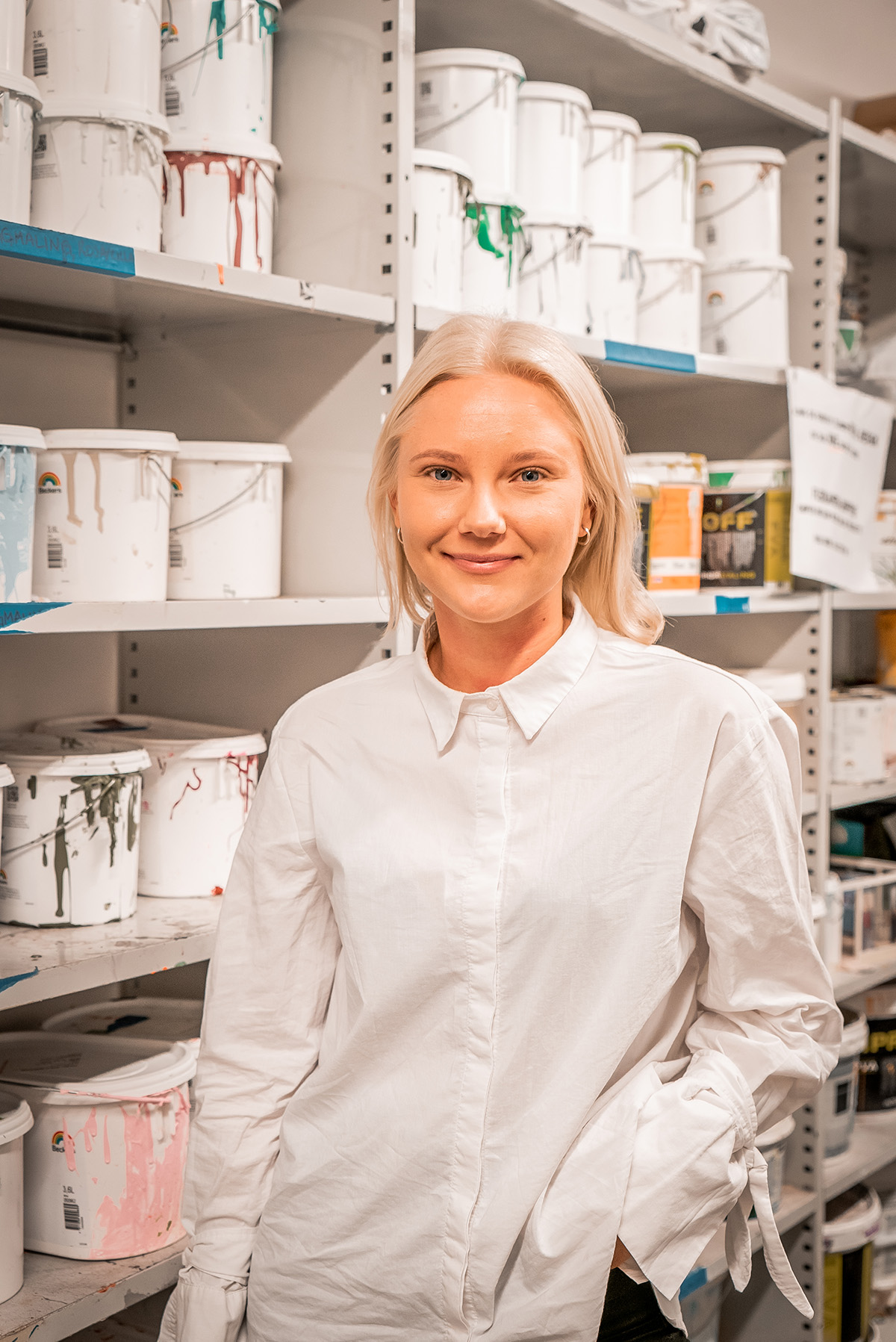 Ida Steffensen står i makerspace på campus Vulkan. Bak henne står det en rekke malespann på hyller. Ida har lyst hår og har på seg en hvit skjorte.