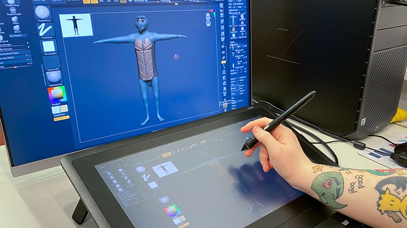 Foto av en student som jobber med et tegnebrett og en pc-skjerm. På skjermen er en animasjonsfigur.