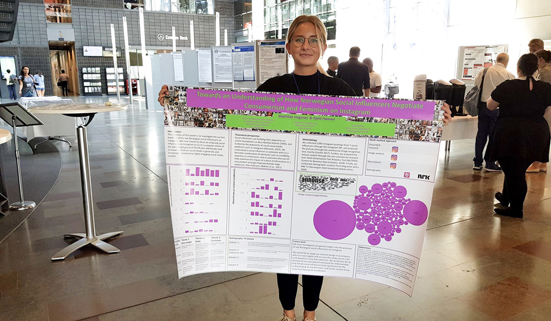 Mathilde Hogsnes vant prisen for Best Poster under International Conference on Social Media and Society Awards i København. På bildet holder hun opp plakaten sin som har grønne og rosa nyanser.