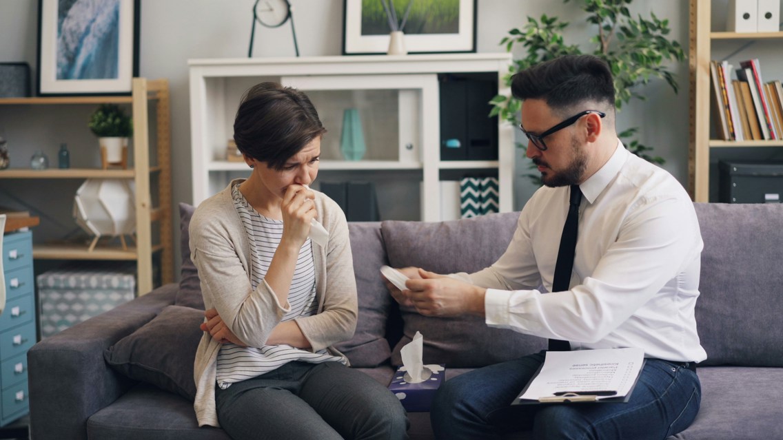 A woman getting some tissue paper from a man sitting on a couch together