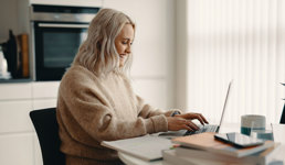 Nettstudent som sitter på kjøkkenet foran laptopen sin og jobber med skolearbeid.