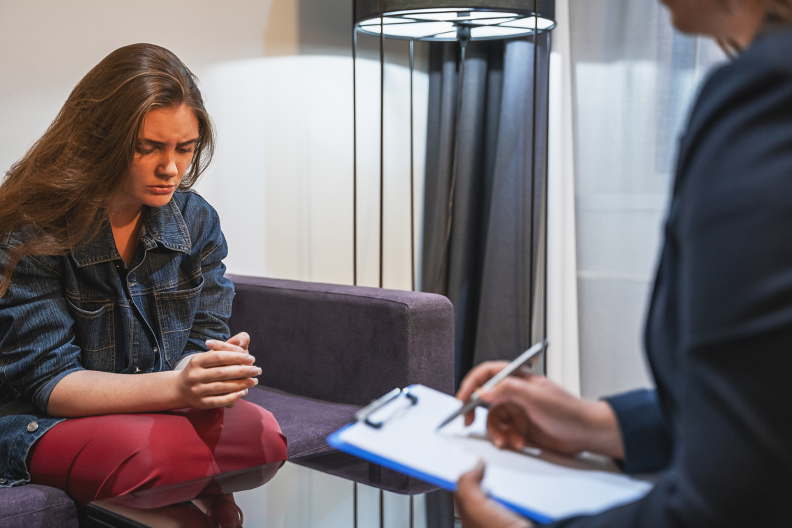 A woman looking upset as she is sitting in a sofa with a man in front of her writing something on a notepad