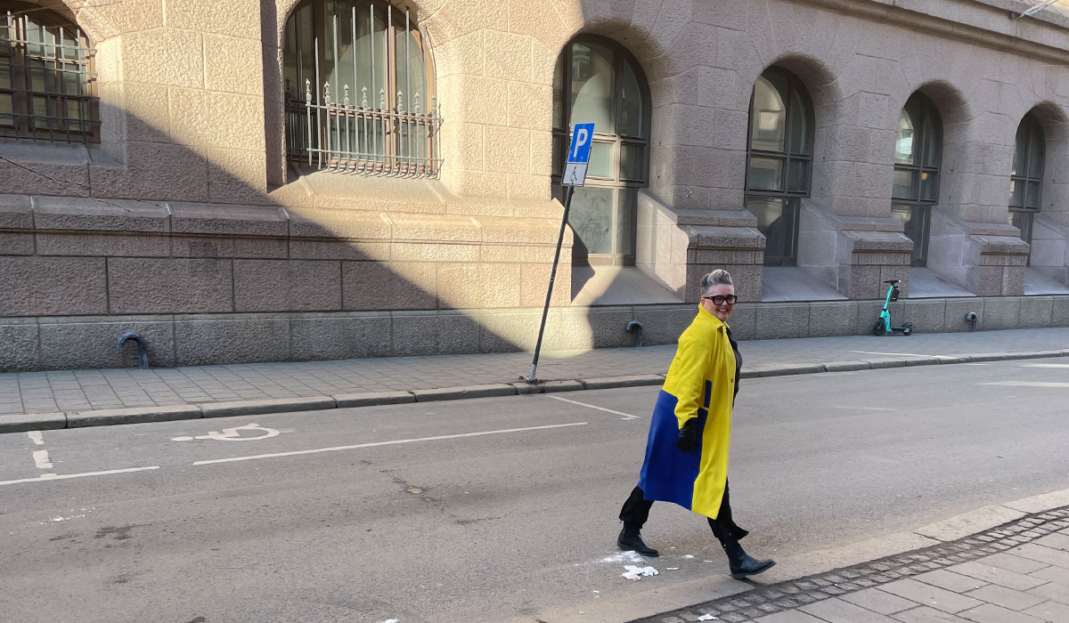 Voksen dame som går over gaten med kåpe i det ukrainske flaggs farger.