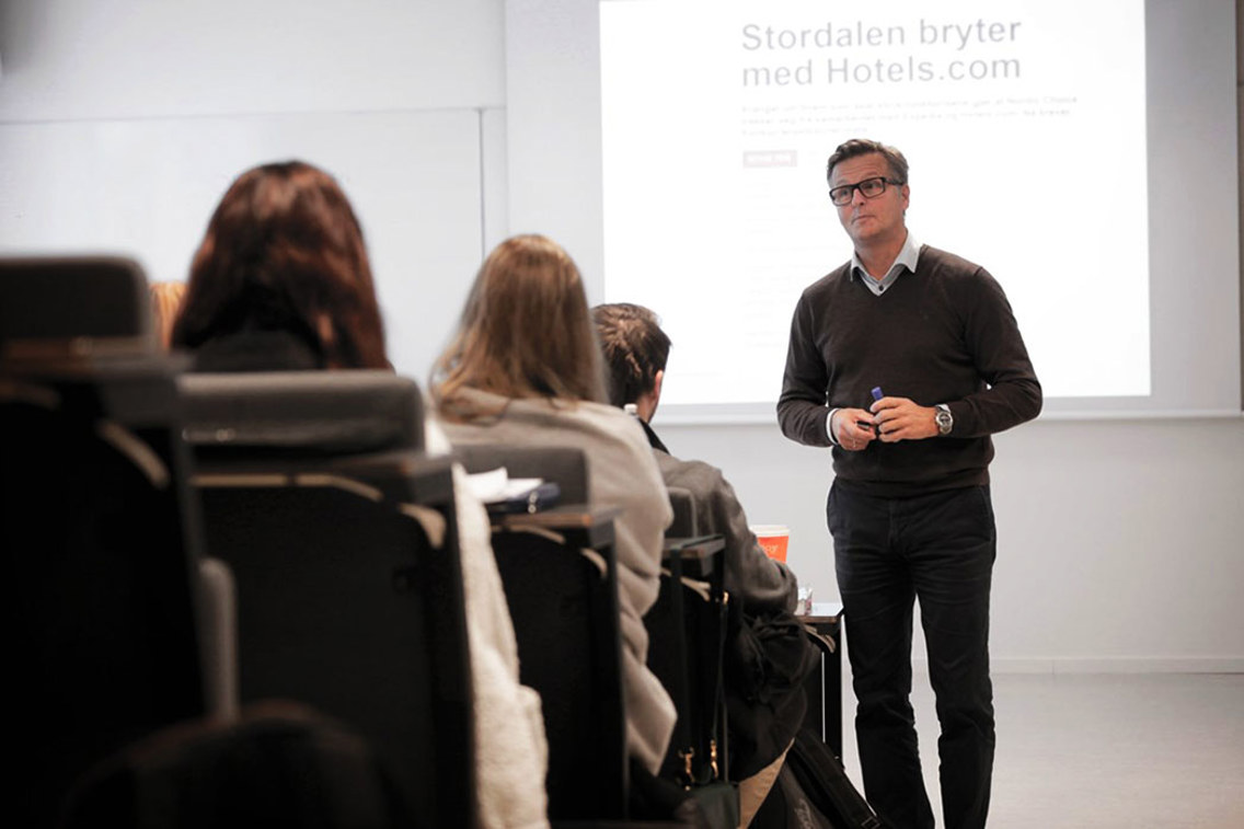 Henning Friberg underviser foran en klasse med en aktiv presentasjon i bakgrunnen. 