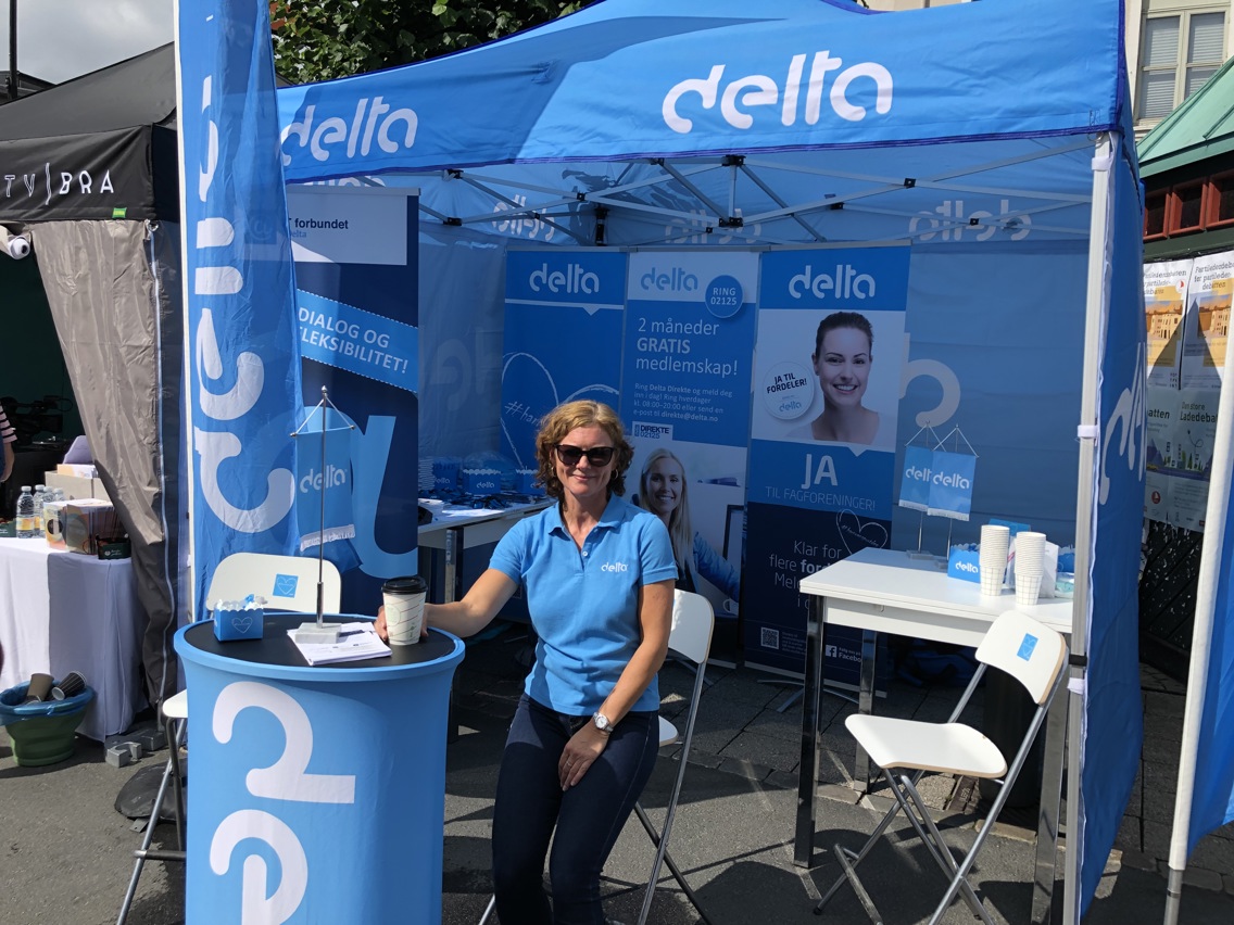 Ina Hebnes sitter på Delta sin stand med solbriller og en kaffekopp i hånden.