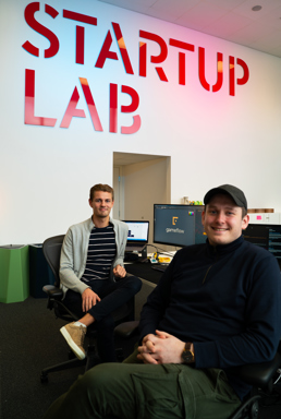Bilde av to unge menn i et kontor med påskriften Startup lab hengende på veggen.