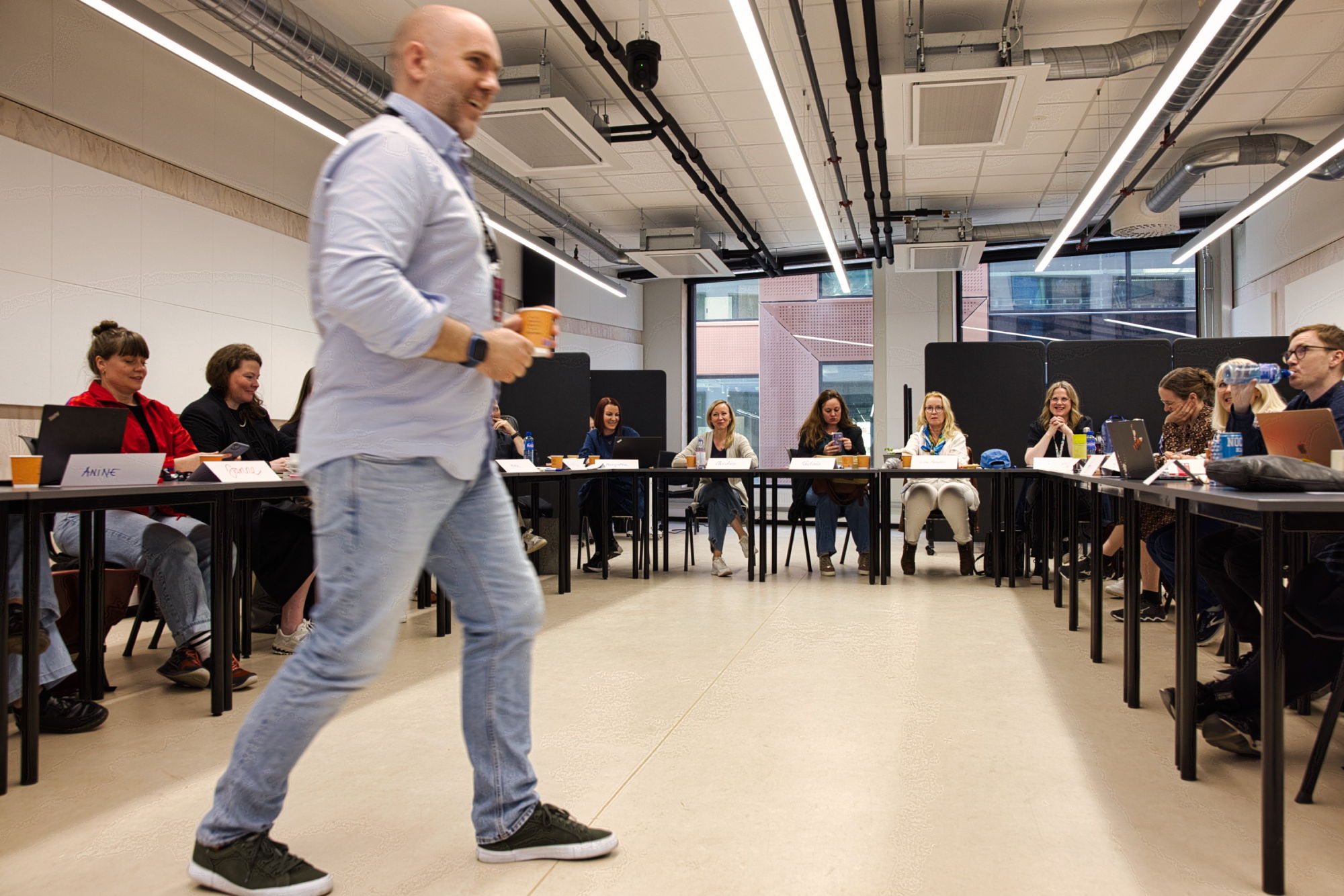 Foreleser snakker til studentene, som sitter med pultene i hestesko rundt ham.