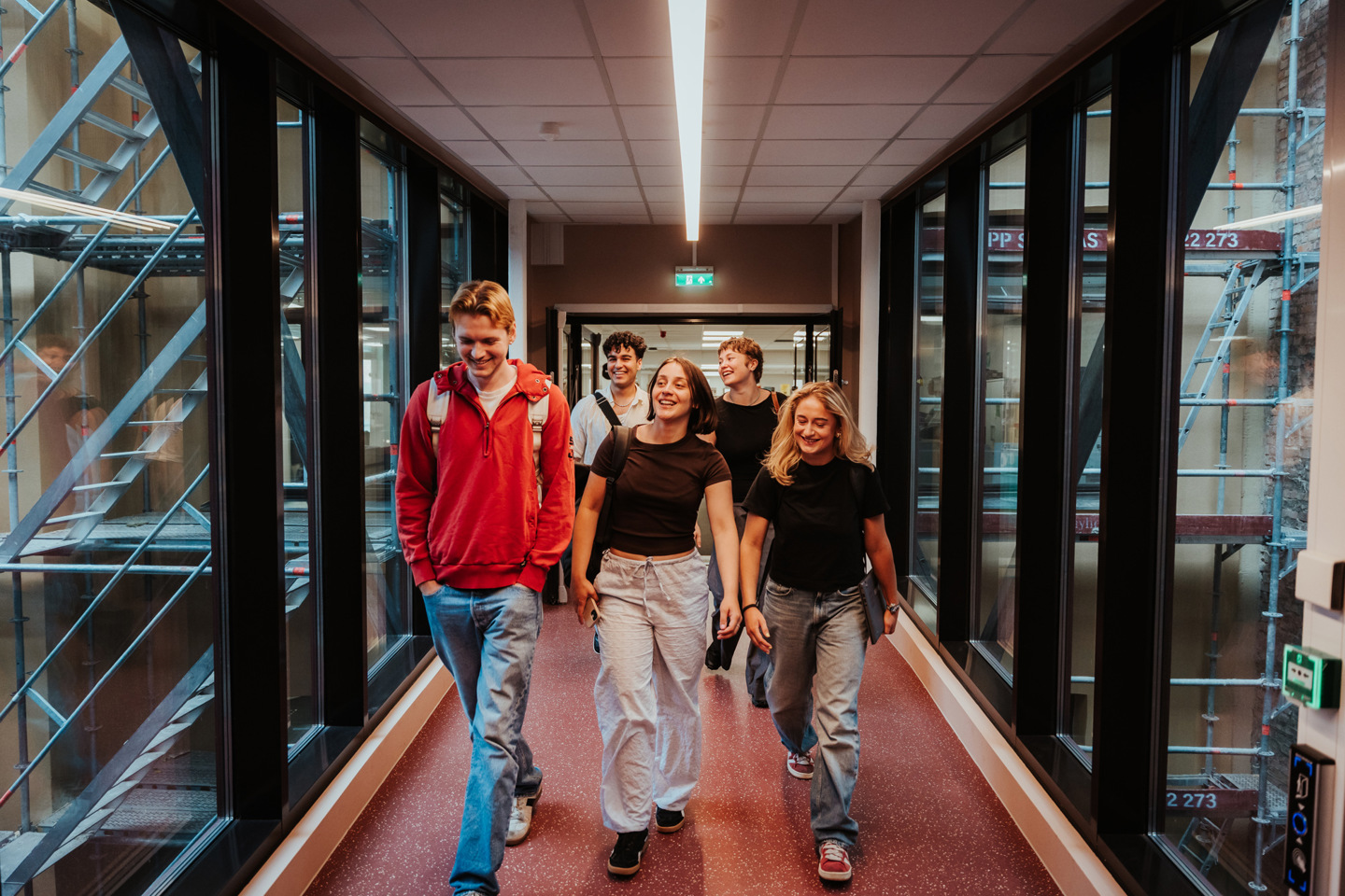 Fem studenter går gjennom en gang med glassvegger på begge sider.