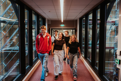 Fem studenter går gjennom en gang med glassvegger på begge sider.