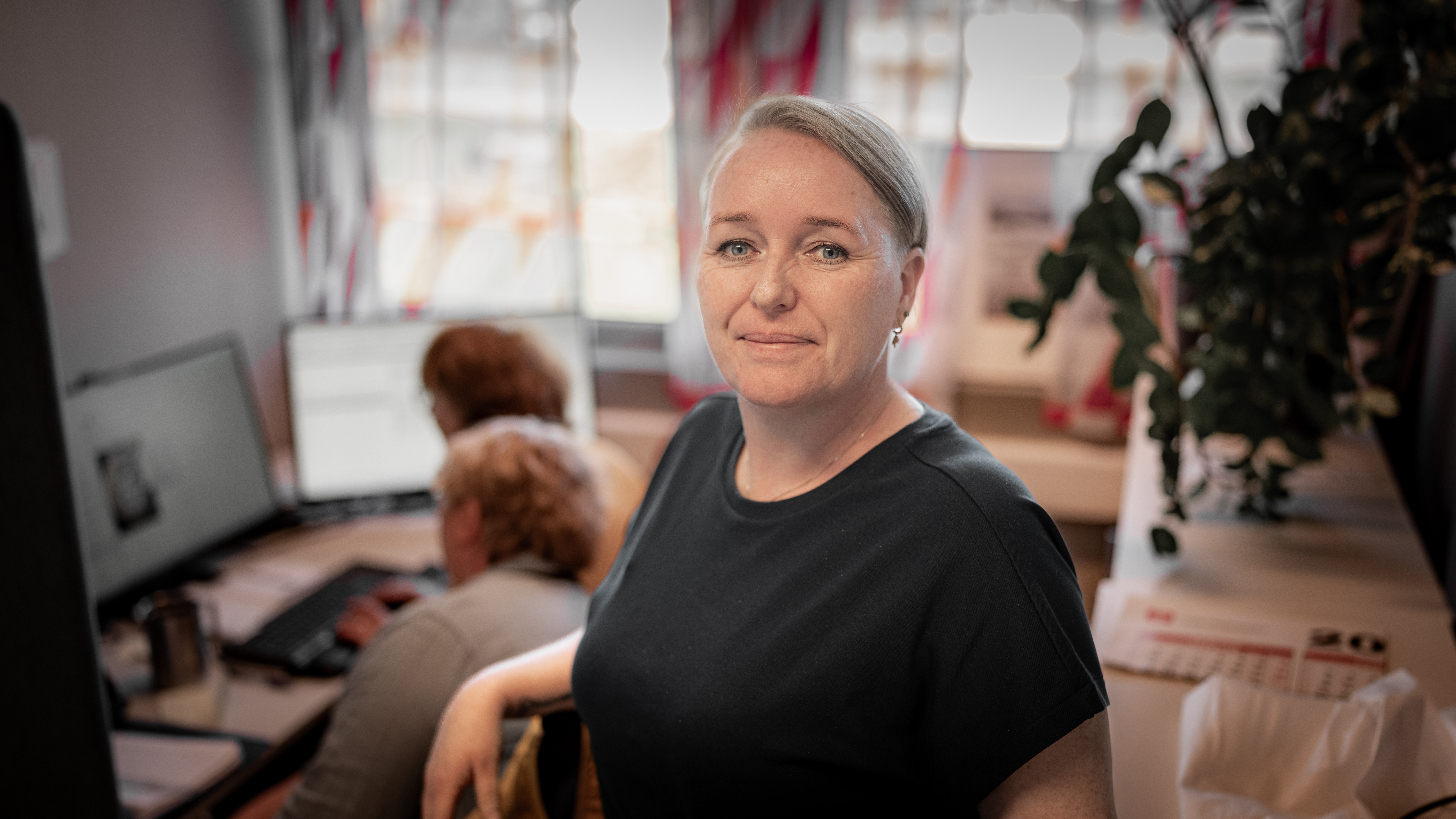 Saksbehandler foran pc smiler i kamera