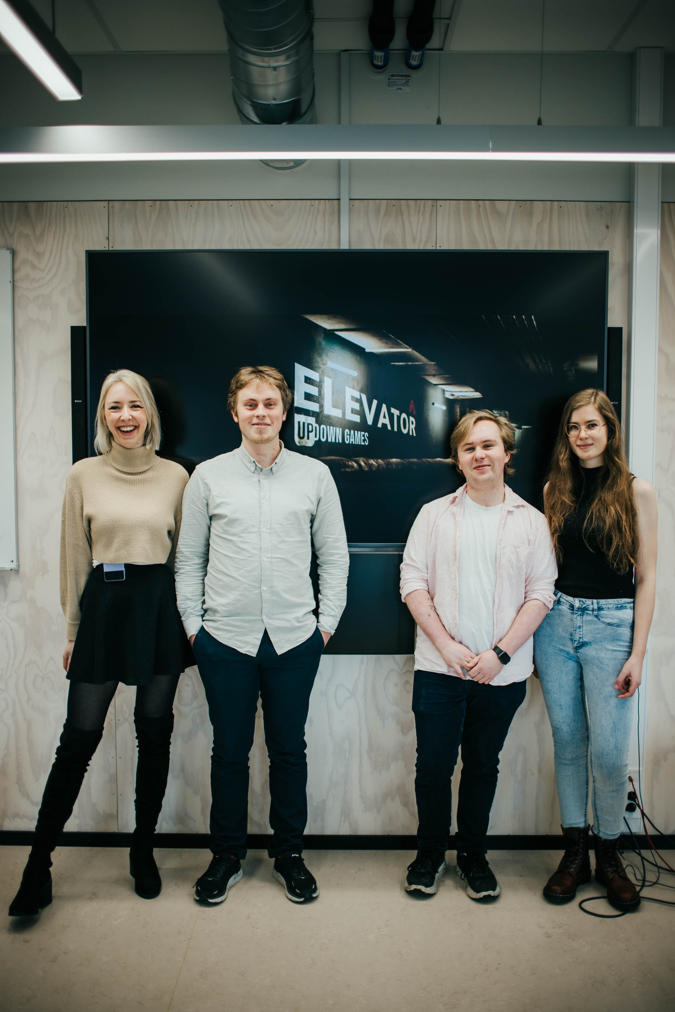 To mannlige og to kvinnelige studenter fotografert foran en vegg.