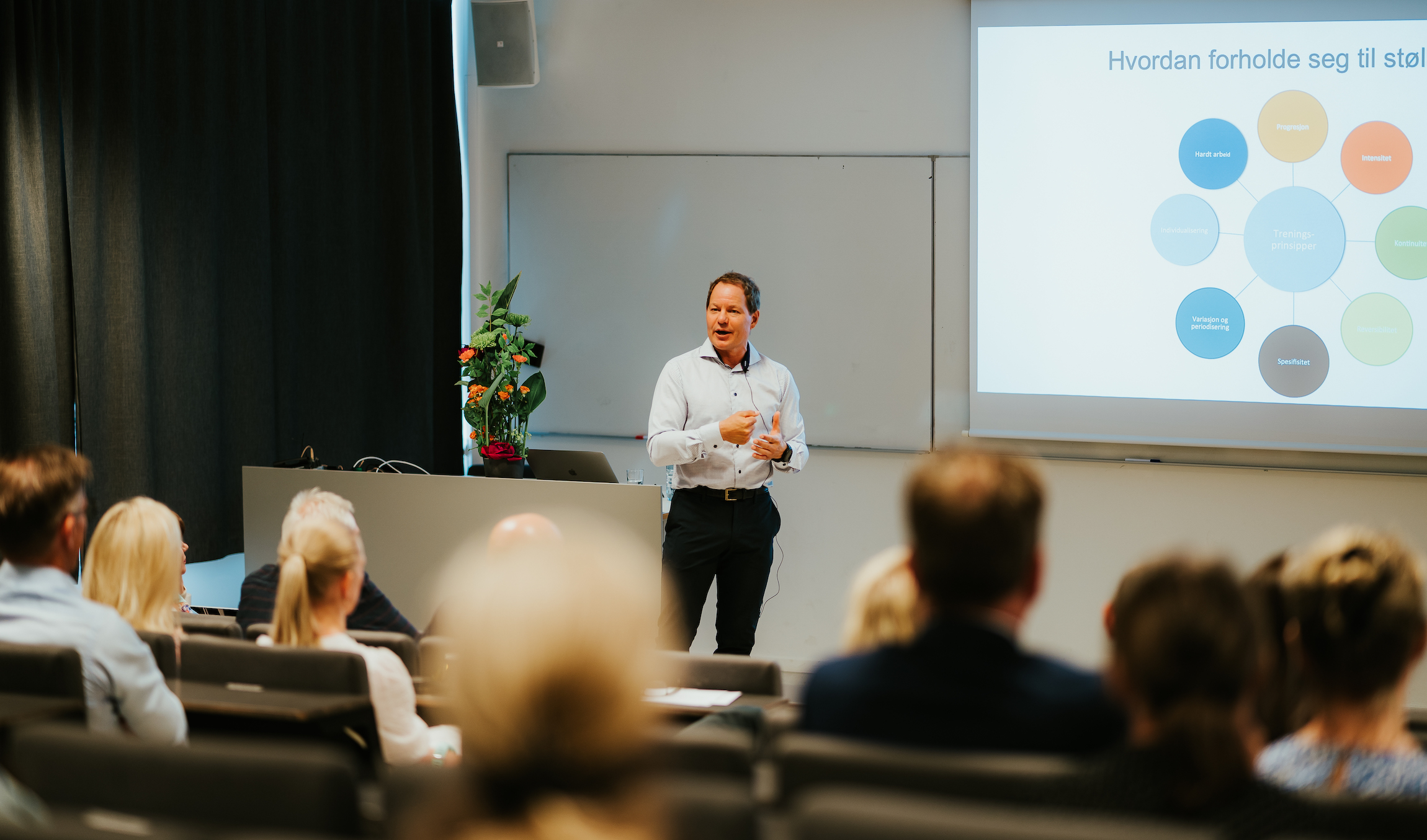 Kalhovde står foran i et auditorium og snakker til mange personer, som sitter med ryggen til.