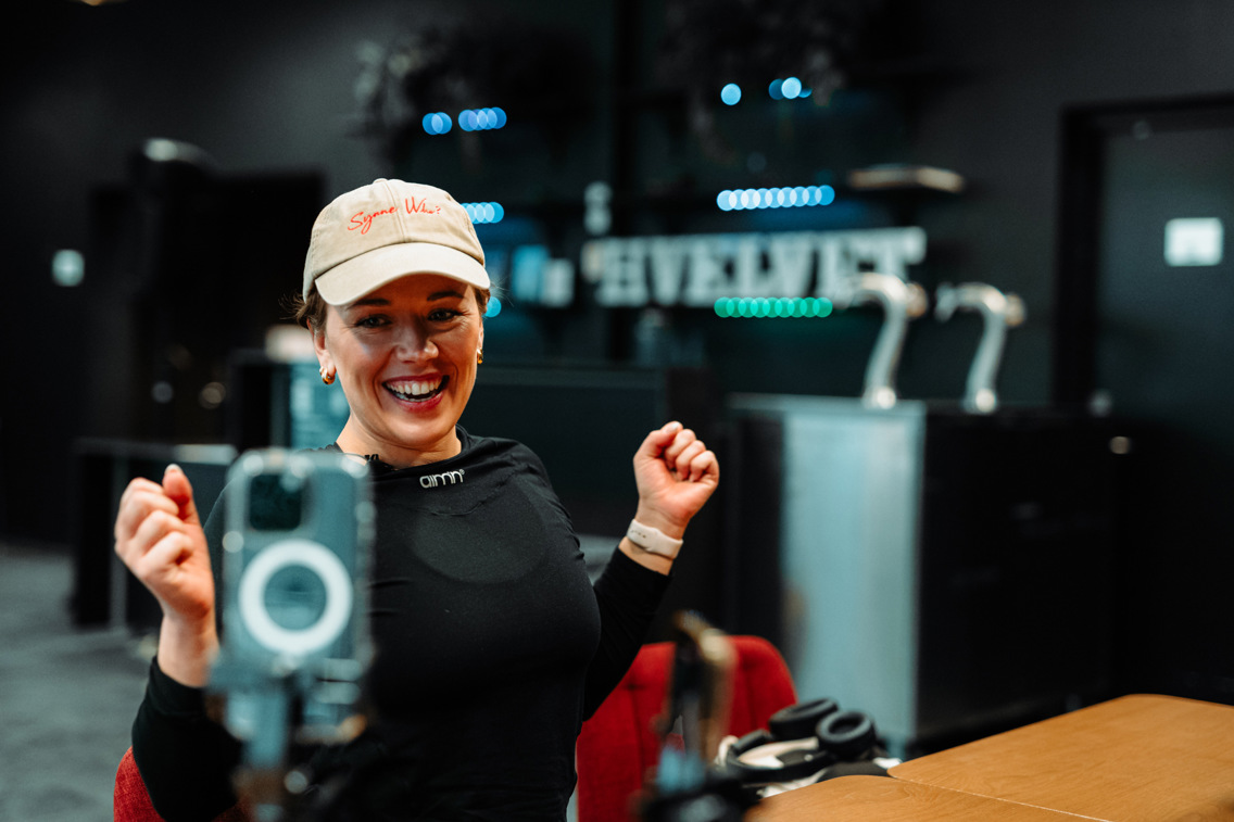 Mathilde Ullum sitter og smiler ved et bord, iPhone på stativ filmer henne