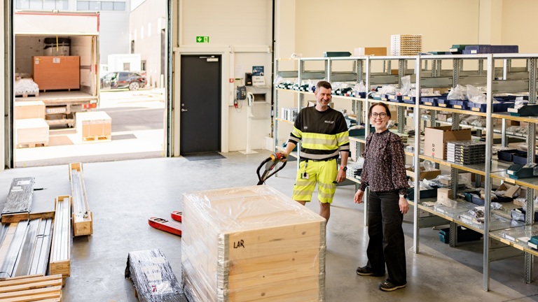 To personer i et lager- og logistikkmiljø blant reoler, varer og utstyr for varehåndtering.