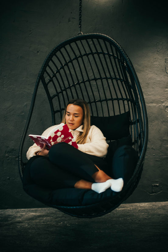 Student sitter i hengestol og leser i en bok.
