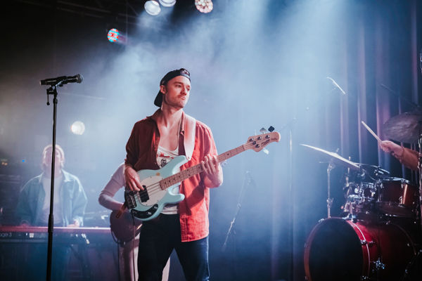 Mannlig student i forgrunnen spiller bassgitar på en konsert.