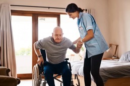 An older man being helped by a nurse to get up from the wheel chair