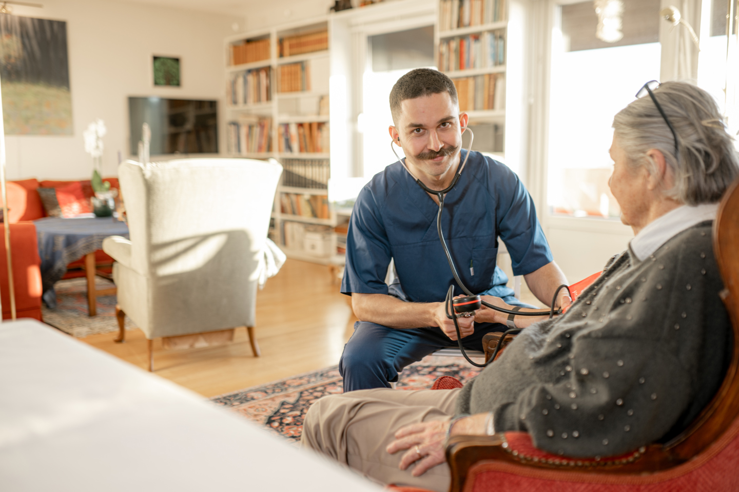 En helsefagarbeider måler blodtrykket til en eldre person i en stue.