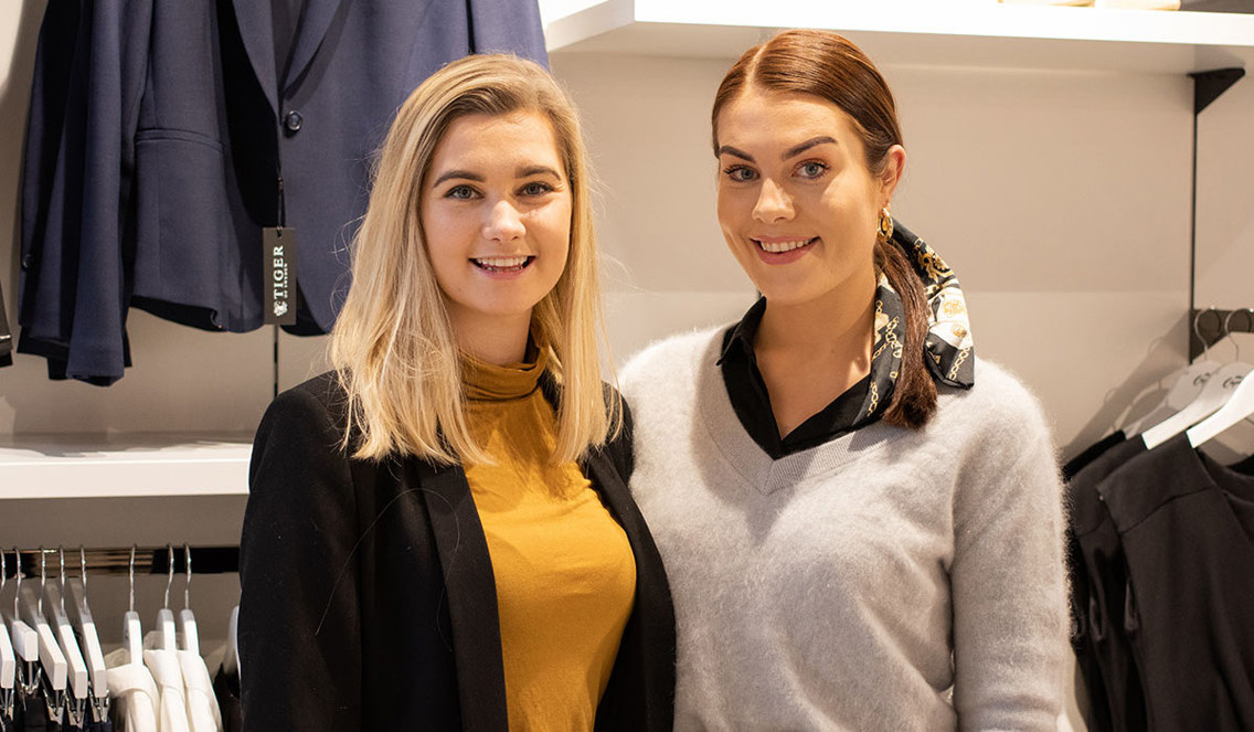 Annika og Pia står ved siden av hverandre i butikken. Begge ser på kamera og smiler.