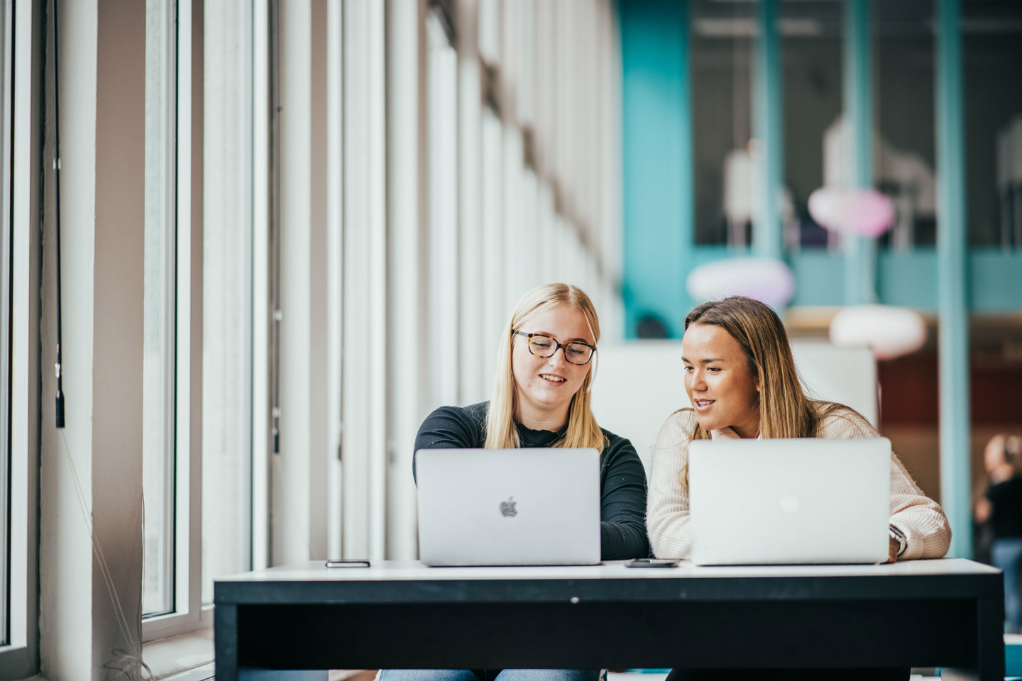 To kvinnelige studenter sitter i et lyst lokale med hver sin mac.