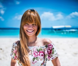 En ung dame smiler inn i kamera mens hun er på stranden