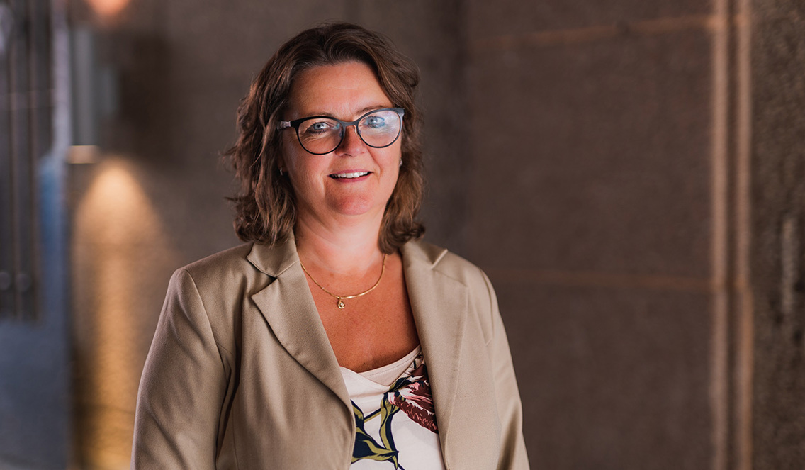 Rektor Annelise Kiønig smiler mot kamera. Hun har halvlangt brunt hår, briller og beige dressjakke. 