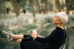 En kvinne sitter ute med en kaffekopp i hånda og bena høyt mens hun sitter og ser ute i lufta