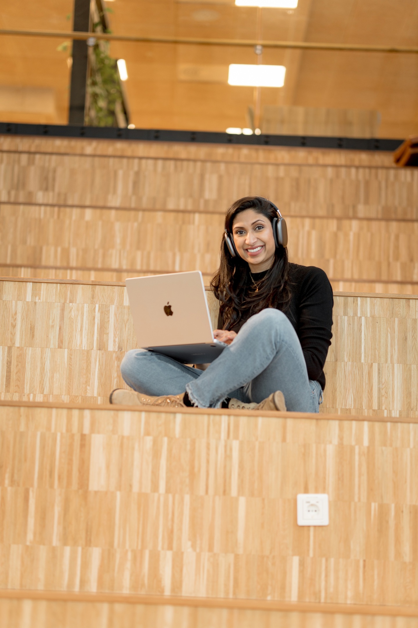 Nettstudent sitter på en trapp inne på Campus med PC og hodetelefoner. 